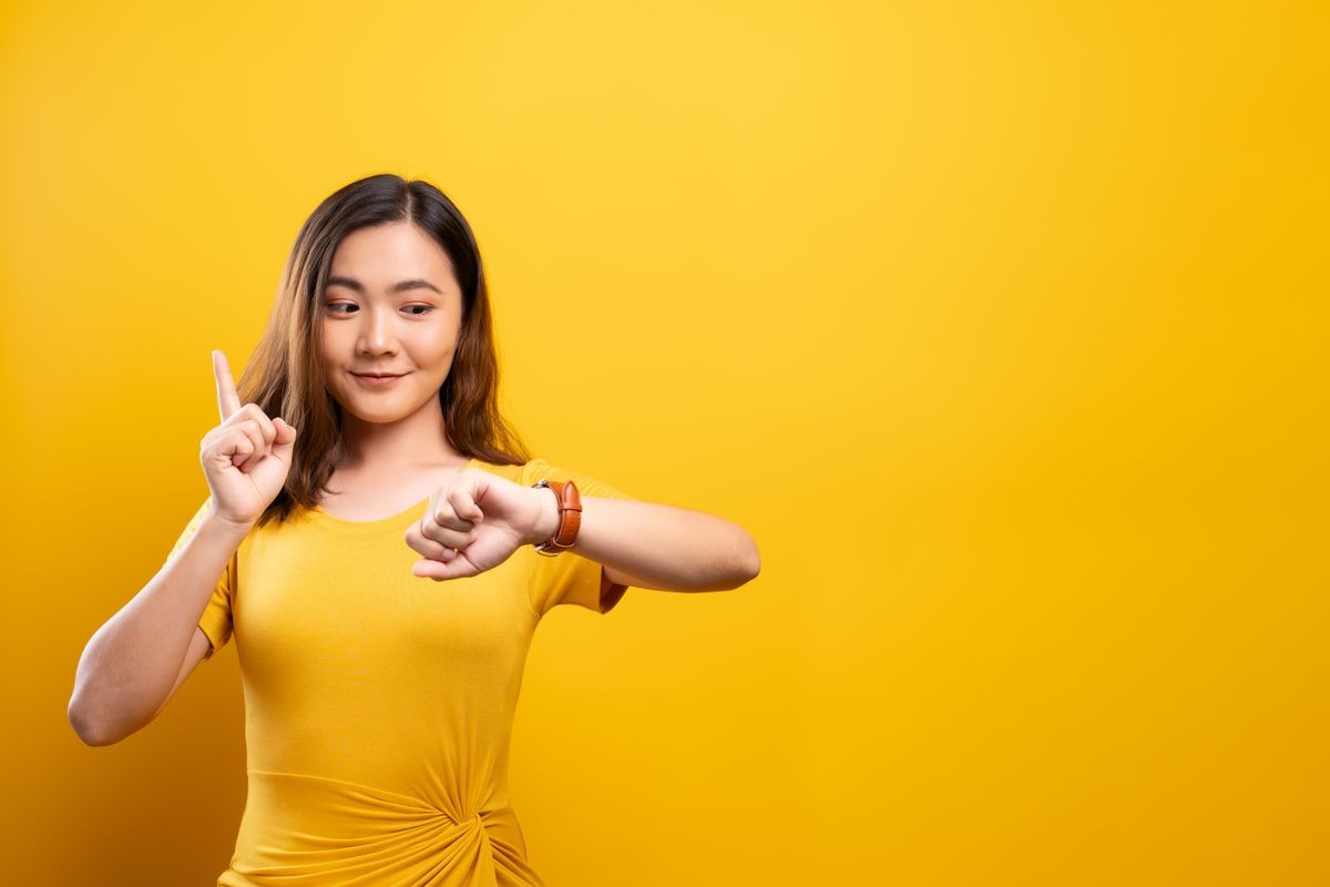Happy woman holding hand with wrist watch isolated on a yellow background